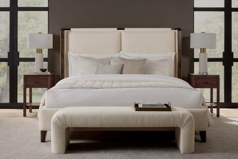 A modern bedroom features the Holden Bed – Leather by James & James with a tall, upholstered headboard. White linens and a plush comforter complement the bed, while solid maple wood nightstands with decorative lamps and a light bench at its foot enhance the contemporary design.