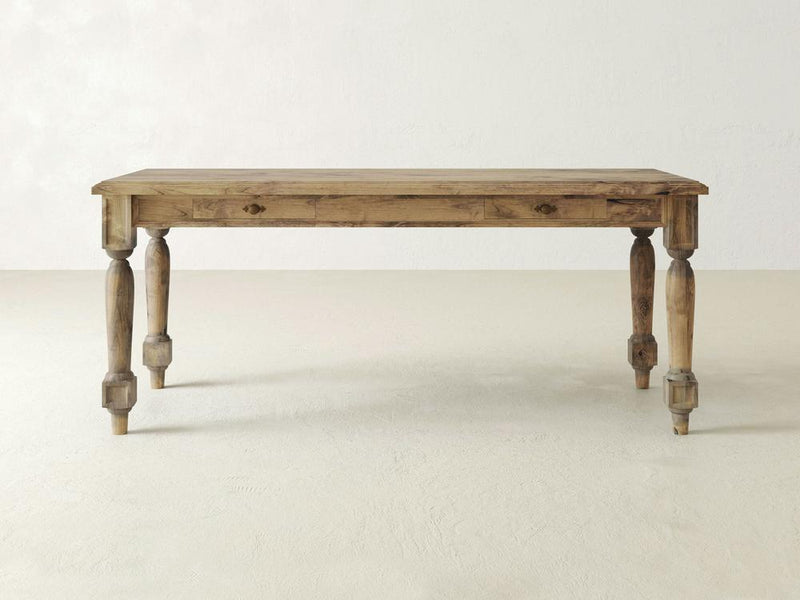 A solid wooden table with a rustic design, the James+James Rosemary Desk features a rectangular top and four thick, turned legs. The wood has a natural, slightly weathered finish, giving it timeless elegance. The table is set against a plain, light-colored background.