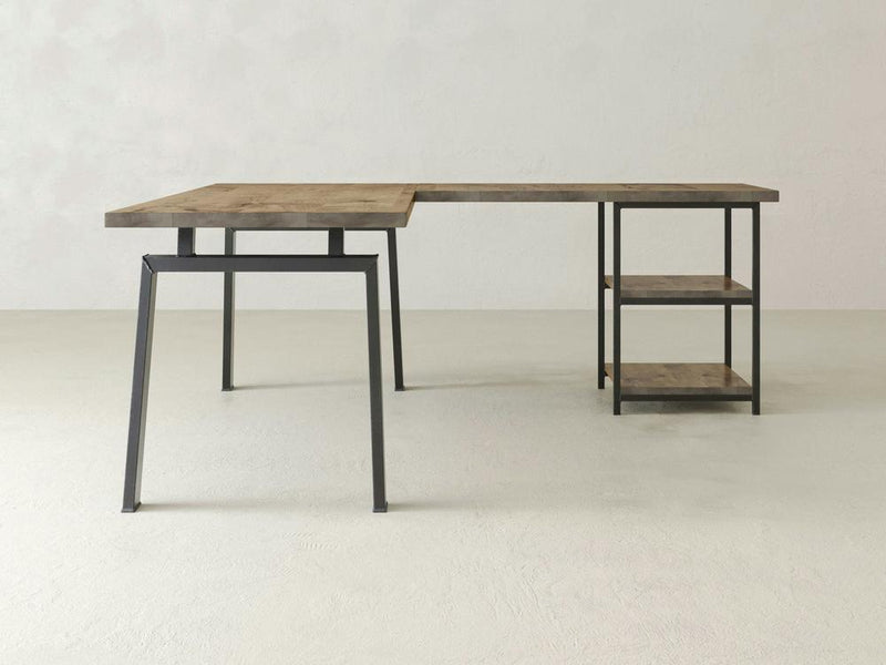 The James & James Fulton Corner Desk in Harvest Wheat features a minimalist L-shape design with a wooden surface and black metal legs against a light gray wall, complemented by two wooden shelves on one side.