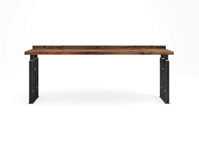 The Clark Sofa Table - Tuscany by James+James showcases a minimalist wooden tabletop adorned with visible grain patterns, elegantly supported by sleek black metal legs. The design exudes a modern and industrial aesthetic, characterized by clean lines and a robust structure.