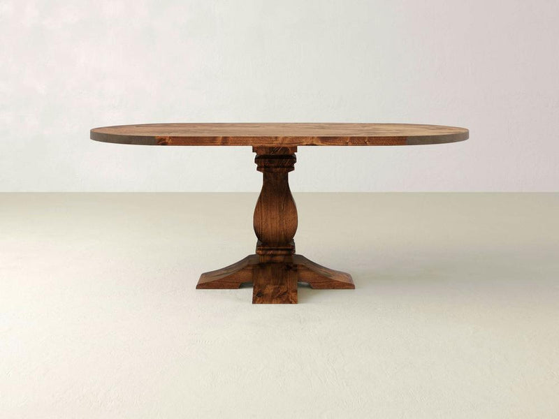 The Heirloom Oval Dining Table - Tuscany by James+James features a smooth surface and an intricately carved pedestal base. It stands on a light-colored floor against a plain background, showcasing its rich brown finish that highlights the natural wood grain.