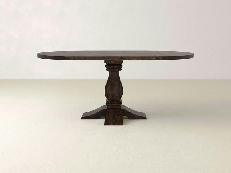 The Heirloom Oval Dining Table by James+James, showcasing an exquisite pedestal design with four supporting feet, features a rich dark finish and a smooth, glossy surface. Set against a plain white background, this wooden masterpiece exudes elegant craftsmanship.