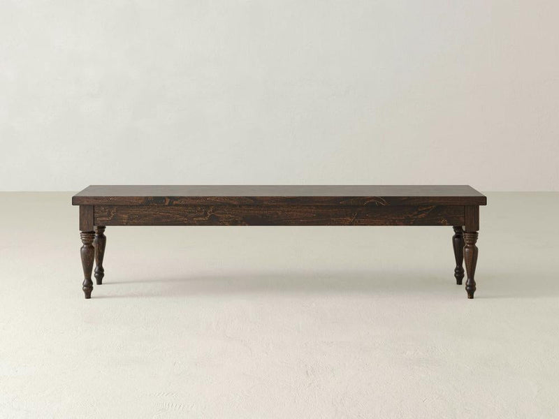 The James & James Chateau Bench - Tobacco features a simple, rustic design with dark wood and four turned legs, set against a plain, light-colored background.