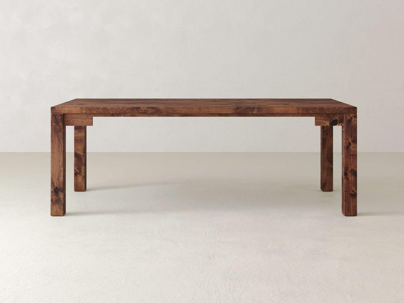 The Jonathan Desk by James+James is a simple rectangular farmhouse-style piece with a natural finish on a light-colored floor. Made from solid hardwood, it features four sturdy legs and a minimalist design that highlights the wood's grain patterns.