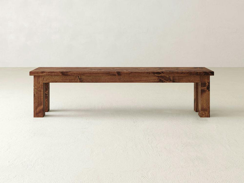 A close-up of the Farmhouse Bench - Tuscany by James+James reveals a wooden surface with a prominent knot in the center. The wood has a rich, warm brown color with visible grain patterns running horizontally. The knot, featuring a dark, irregular shape, adds texture and character to this beautifully crafted piece.