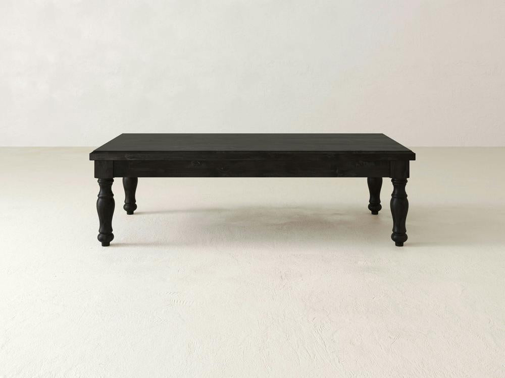 The Abigail Coffee Table in Charred Ember from James+James, a robust piece crafted from dark wood with intricately designed legs, stands on a light-colored floor against a plain white background. The table features a simple, rectangular shape and boasts a smooth, polished surface.