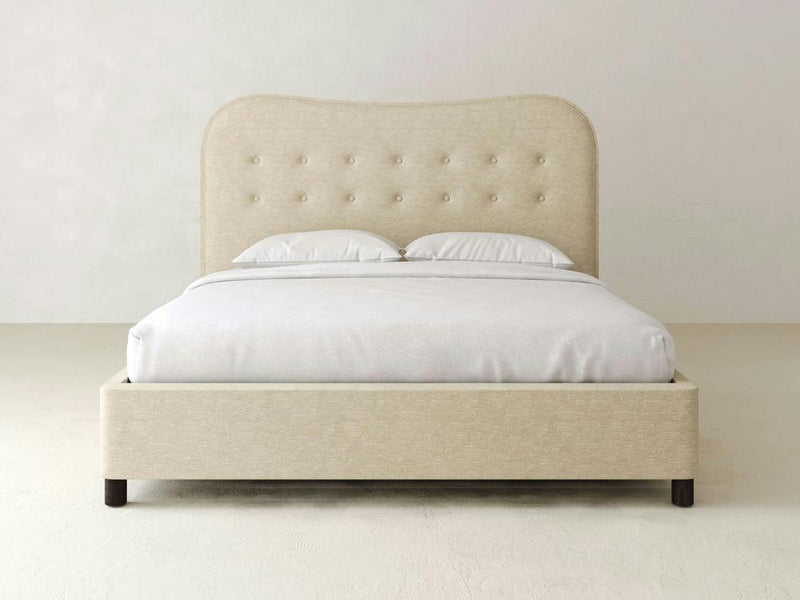 The James & James Florence Bed – Linen offers a timeless appeal with its beige upholstered frame and high, slightly curved headboard featuring button tufting. Paired with performance linen bedding in crisp white, it sits elegantly against a plain, light-colored wall and floor.