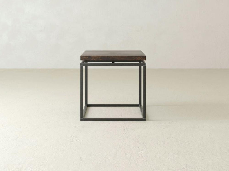 The Floating Top End Table - Tobacco by James+James, a minimalist and modern piece, features a square dark wooden top paired with a black metal frame. It sits against a plain, light-colored background showcasing its simple design with clean lines and an open base.