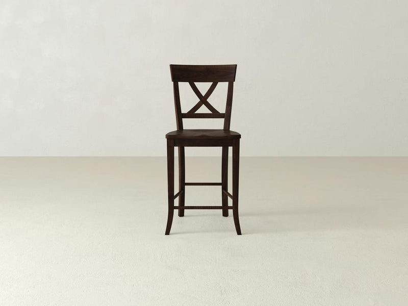 The Juniper Stool by James & James, made of rich maple hardwood, features an X-back design with a slightly curved seat and practical footrests, set on a light, neutral-colored floor against a plain background.