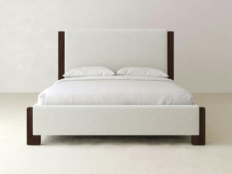 The Lennon Bed – Boucle by James & James showcases a minimalist design with a white upholstered boucle headboard and footboard. Complemented by white sheets and pillows against light walls and flooring, it exudes serenity with subtle maple accents for warmth.