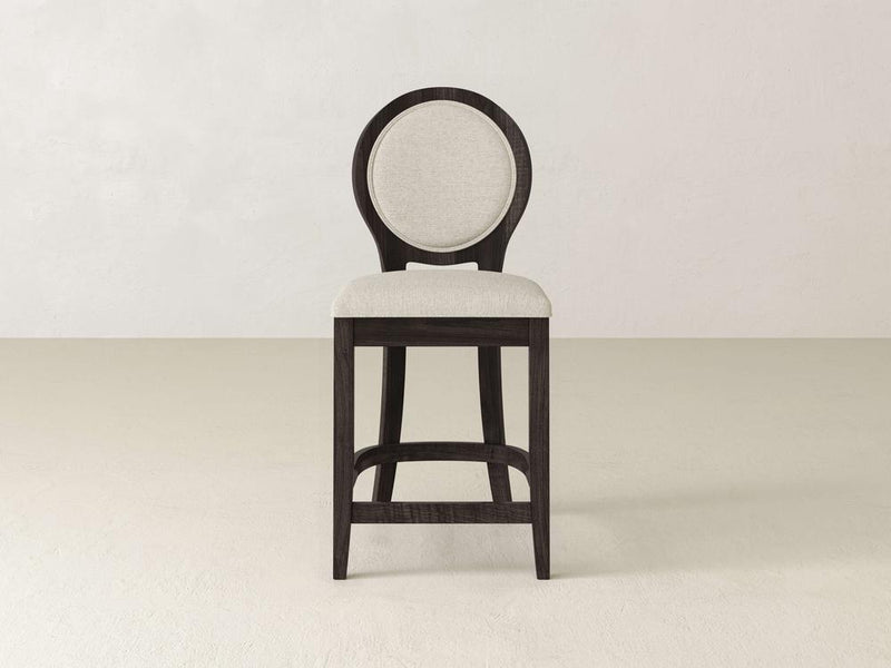 The Alice Stool by James & James showcases modern elegance with its tall dark maple wood frame and circular backrest, upholstered in light beige fabric against a plain, light-colored backdrop.
