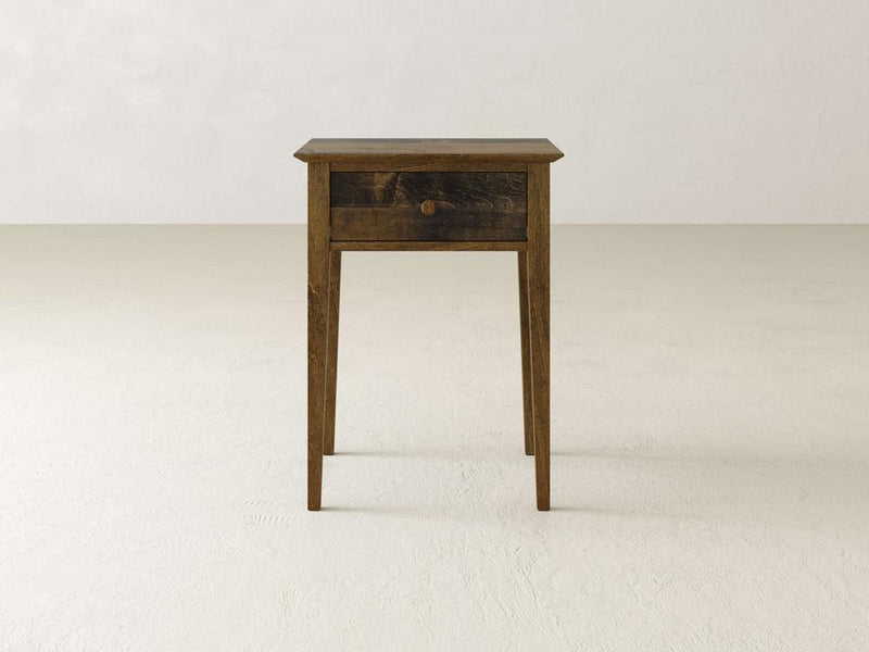 The Bennett 1 Drawer Nightstand by James & James is a small, rustic piece made from solid maple wood. It features a single drawer and slender legs, perfect for a bedroom, and is displayed against a plain, light-colored background.