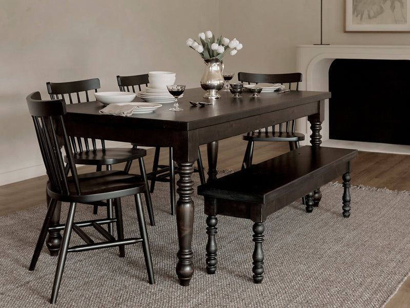 The James+James French Country Dining Table in Harvest Wheat, paired with matching chairs and a bench, sits on a textured rug. Set with plates, glasses, and white tulips, the room features neutral walls and minimal, elegant decor.