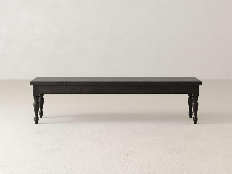 Against a plain white background stands the Chateau Bench by James & James, a long dark wooden piece with carved legs. This handcrafted bench offers a simple, classic design and four decorative legs, perfect for adding elegant dining seating that blends style and function.