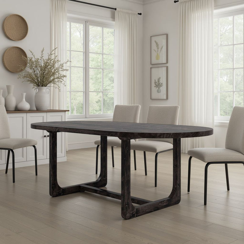 A modern dining room featuring the James+James Emersen Oval Dining Table in Charred Ember, four light upholstered chairs, white walls, large windows with sheer curtains, and minimalist decor like vases and botanical prints.