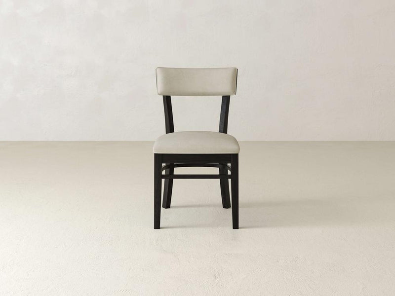 The Everly Side Dining Chair Set of Six by James+James features a mid-century design with a Charred Ember wooden frame and Cream cushioned seat and backrest, standing elegantly on a light-colored floor against an off-white wall.