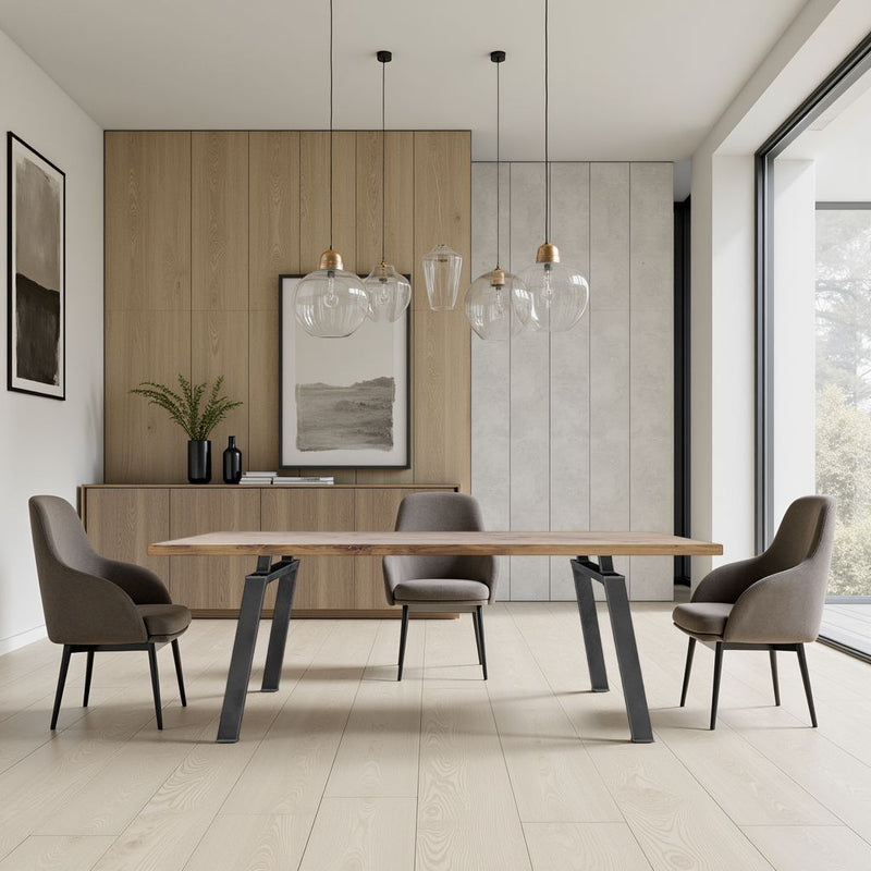 A modern dining room featuring the James+James Fulton Dining Table in Harvest Wheat, four upholstered chairs, pendant lights, light wood floors, large windows, and minimalist decor with framed art and a vase of green foliage.