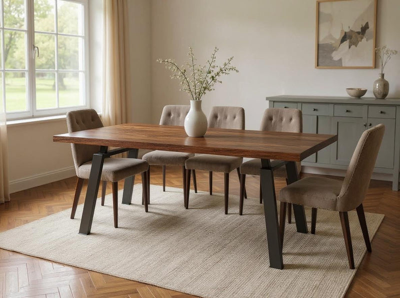 A modern dining room featuring the James+James Fulton Dining Table - Tuscany, six cushioned chairs, a sideboard, a large window with light curtains, and a white vase with branches as a centerpiece on a beige rug.