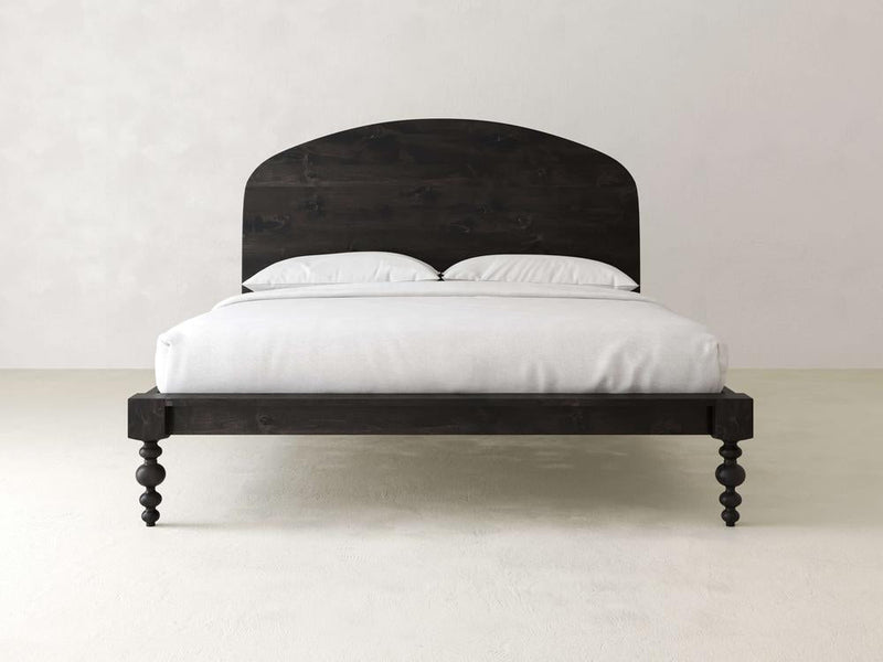 A minimalist bedroom showcases the Olivia Arch Bed - Charred Ember from James+James, featuring a rounded headboard and uniquely carved legs. It's neatly dressed with smooth white bedding against plain light-colored walls and floor.