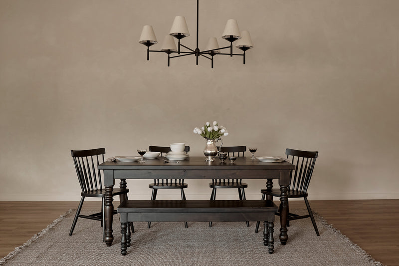 A minimalist dining room features the James+James French Country Dining Table in Harvest Wheat, four matching chairs, a bench, set with dishes and a vase of white flowers. A modern chandelier hangs above, with a neutral rug on the wooden floor.