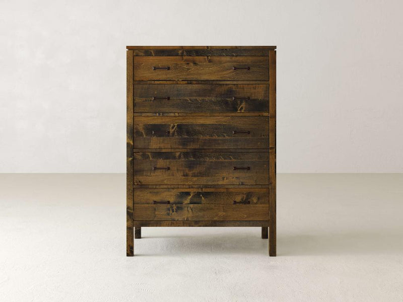 The James & James Jensen Tall Chest, made from solid maple hardwood, features a rustic yet slightly weathered finish. Its five drawers have simple metal handles that complement contemporary designs against a plain, light-colored backdrop.