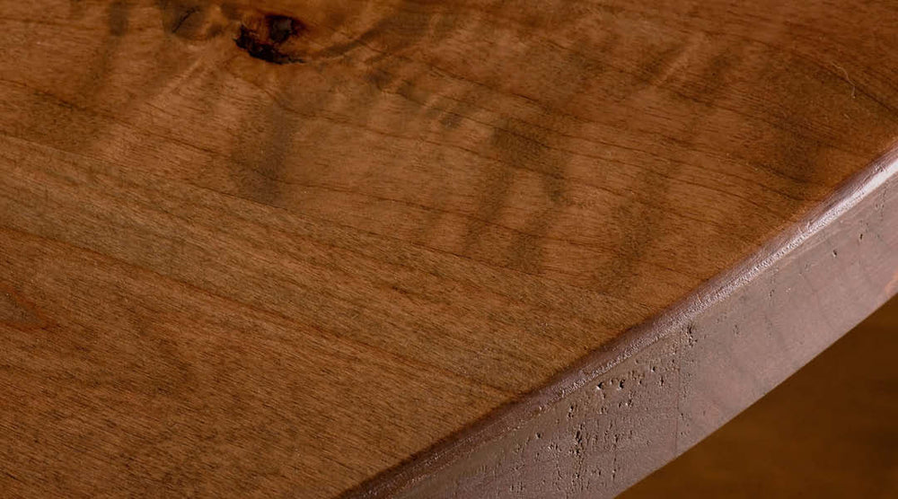 Close-up of a wooden surface with a smooth finish and visible natural grain patterns. The wood has a warm brown tone, and the edge shows precise craftsmanship.