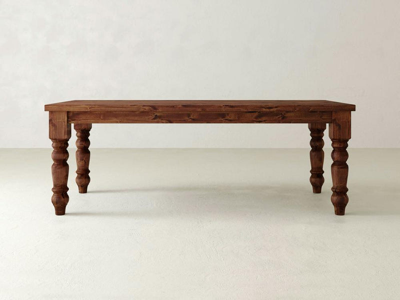 Introducing the James+James Baluster Dining Table: Featuring intricately carved, turned legs and a smooth, polished surface, this table is expertly handcrafted from fine wood. Set against a plain, light-colored background, its design exudes a timeless classic and rustic charm.