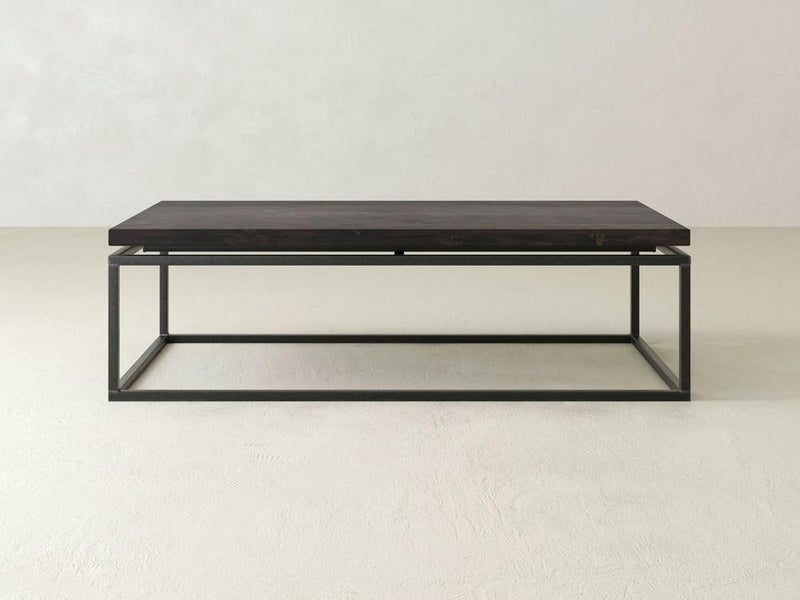 A rectangular coffee table, the "Floating Top Coffee Table - Charred Ember" by James+James, features a dark wooden top paired with a minimalist black metal frame. The table boasts a simple, modern design and is set against a plain, light-colored background.
