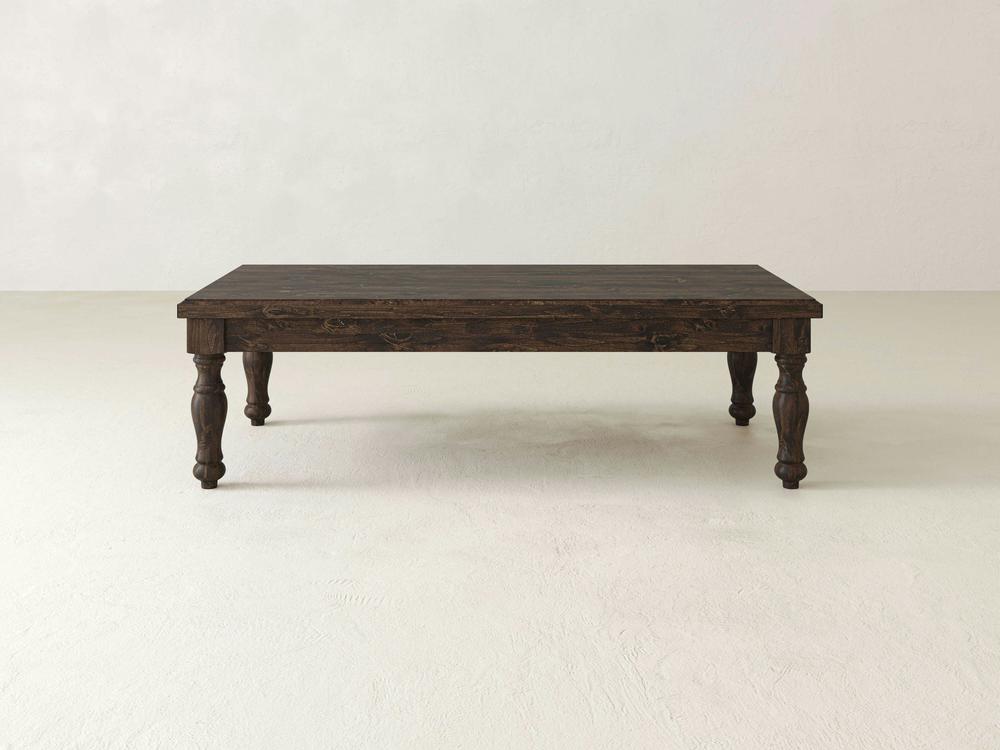 The Abigail Coffee Table - Tobacco by James+James, a dark wooden rectangular table with four intricately carved legs, stands on a light-colored surface against a plain background.